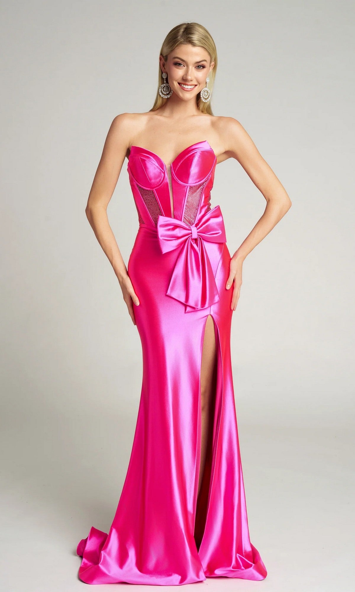 A woman poses against a plain background in the Portia and Scarlett PS26136 long formal dress, featuring fuchsia satin, a strapless corset bodice, mesh side panels, and a thigh-high slit.